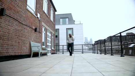 casual businessman walking on rooftop terrace talking on mobile phone and drinking coffee