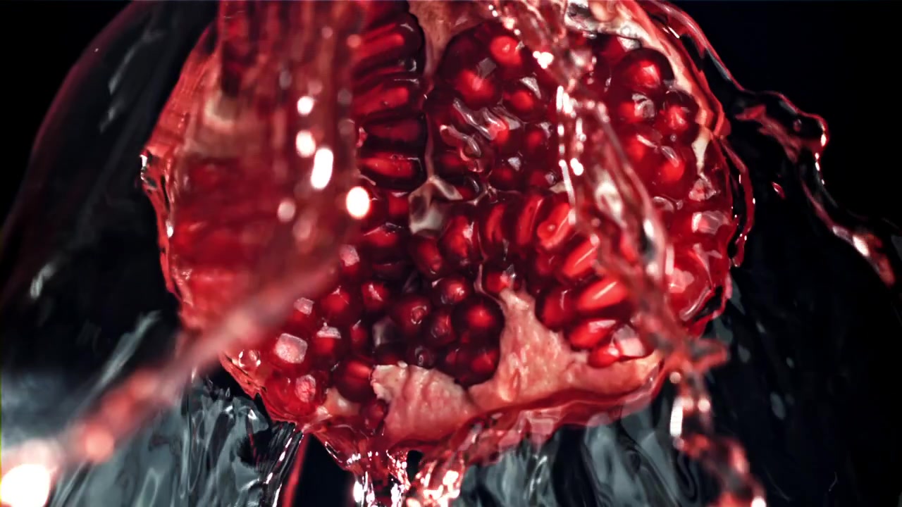 Slowmotion: Vand sprøjter på en frisk granatæblehalvdel.