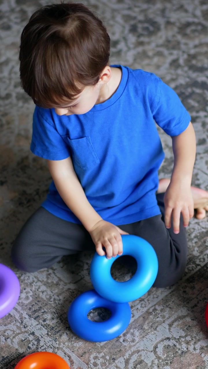 Un niño pequeño se sienta en el suelo jugando con una pirámide. Un niño adorable jugando tranquilamente en casa. Vista superior. Video vertical.