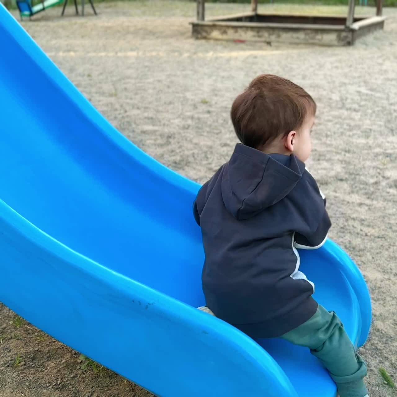 Caucasian toddler in hoodie walks up to the slide. Baby boy tries to climb up by the slide but goes down