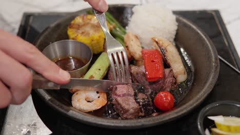 cutting roasted beef steak served with white rice, grilled prawns, and vegetables