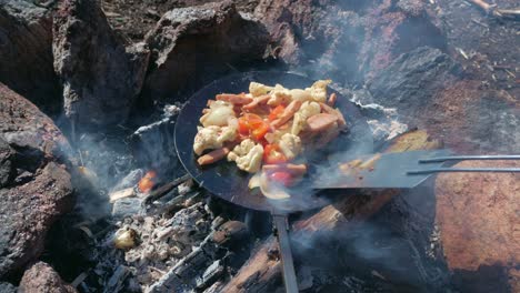 hands cooking food on campfire with a cast iron pan and spatula