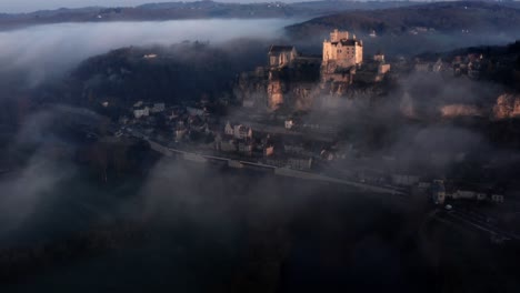 beautiful cinematic aerial view of beynac castel above the fog and river in sunrise light, dordogne france, blue mood