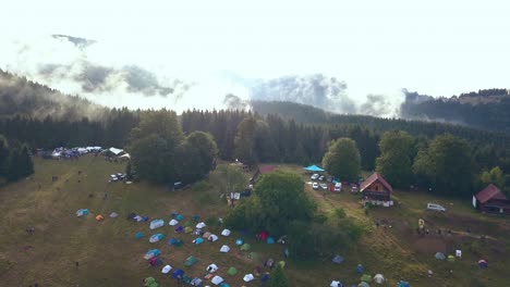 Tiro-Aéreo-Inclinado-De-Drones-Que-Revela-Un-Campamento-De-Festival-Rumano-Con-Una-Hermosa-Cadena-Montañosa-Como-Telón-De-Fondo