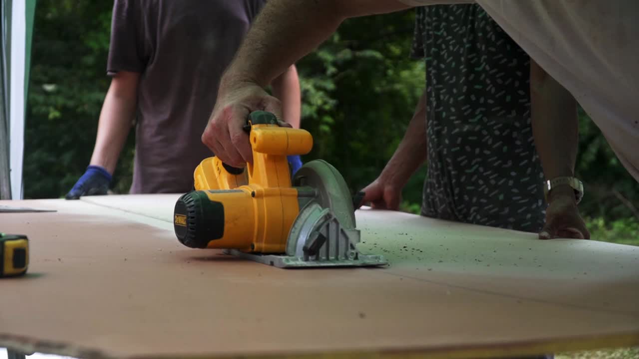 Building contractor worker using hand held worm drive circular saw to cut boards on a new home constructiion project