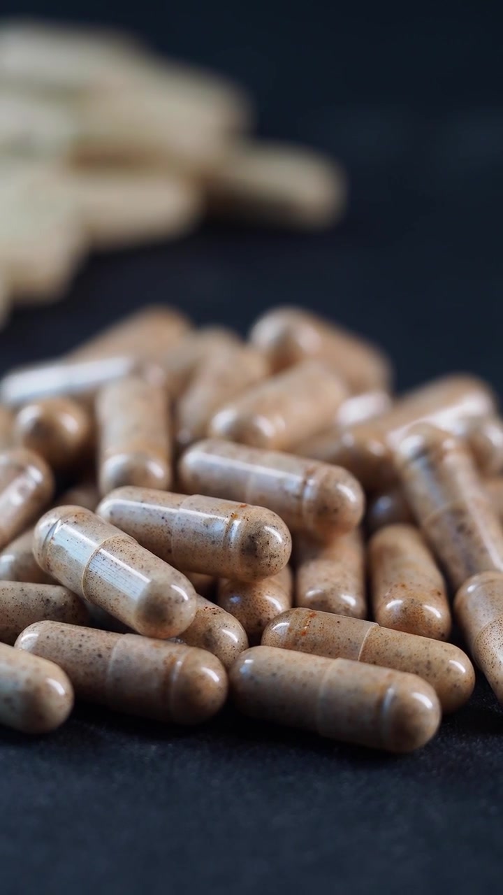 Pila di capsule marroni di integratori erboristici su sfondo scuro