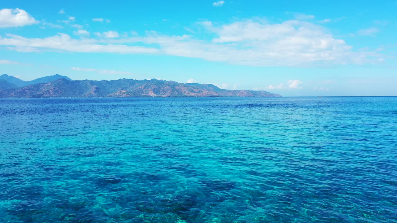 Crystal emerald azure water over corals and pebbles, reflecting sunlight of bright morning sky with hanging clouds in Indonesia