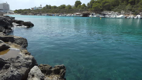 scenic view from water level at noon of cala santandria creek in menorca with yellow boat markers, blue transparent sea and surrounding rocks