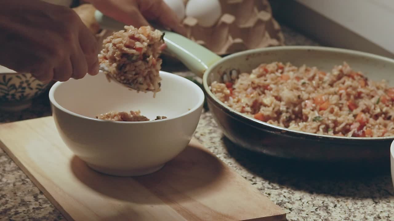 Serving a newly cooked vegetable fried rice on to a white bowl showing a candid kitchen scene and daily home cooking