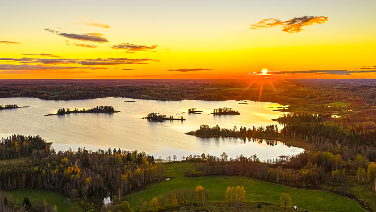 Kimaltava auringonlaskun hehku heijastuu tyynestä lammesta, kun metsän reuna tummenee illan väriloistoon.
