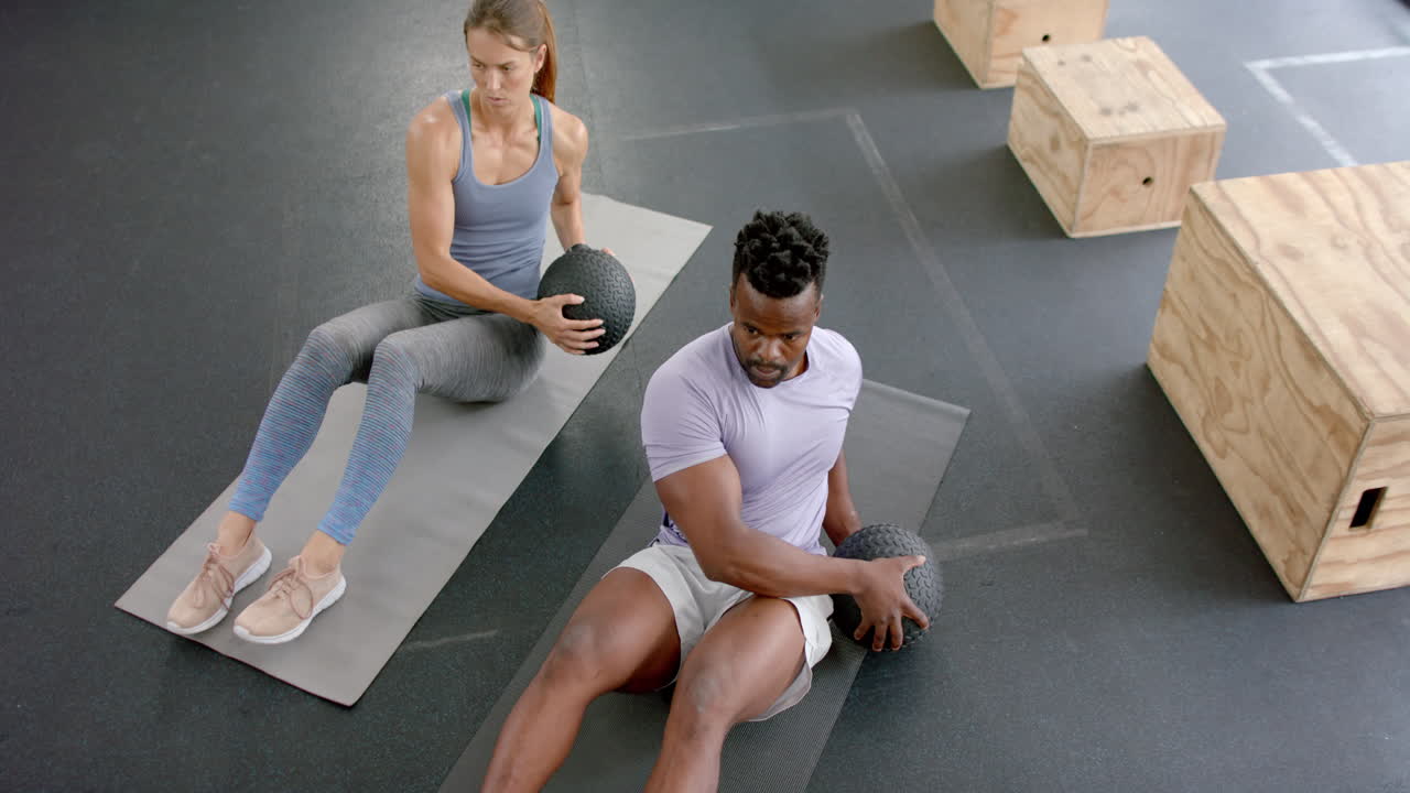 Fit young Caucasian woman and African American man exercising at the gym with medicine ball