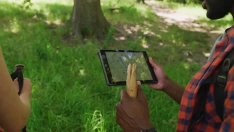 Diverse-couple-hiking-with-backpacks-and-using-tablet-with-map-in-park,-slow-motion