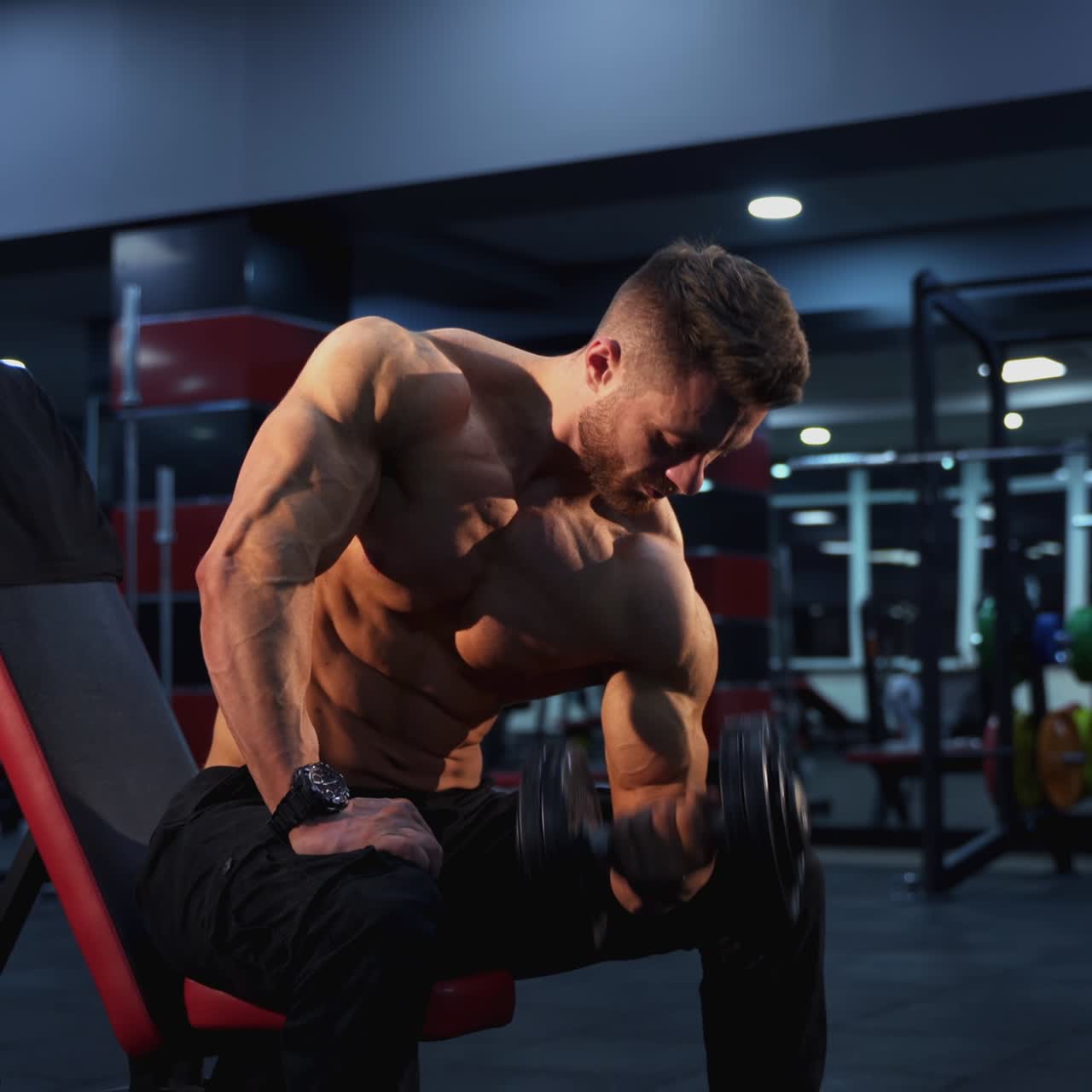Atleta muscoloso con un manubrio. Forte e bel sportivo a torso nudo che allena i bicipiti del braccio con attrezzatura sportiva in palestra.