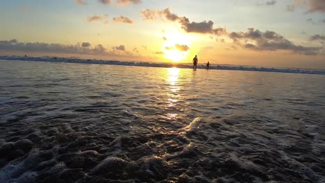 Olas-Que-Fluyen-A-Tierra-En-La-Playa-En-Una-Puesta-De-Sol-En-Bali,-Indonesia,-Mientras-El-Sol-Se-Pone-Dorado-Hermoso