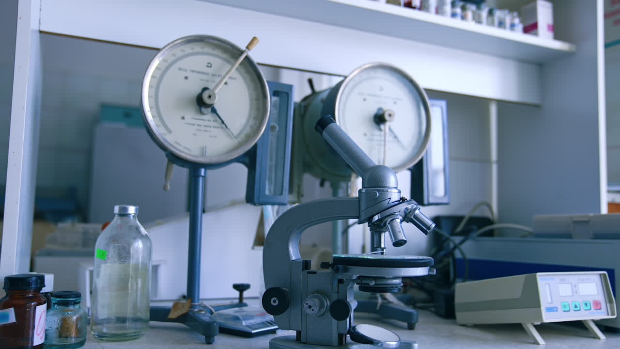 Old-fashioned microscope on the table of medical laboratory. Tools and appliances on the shelves at backdrop.