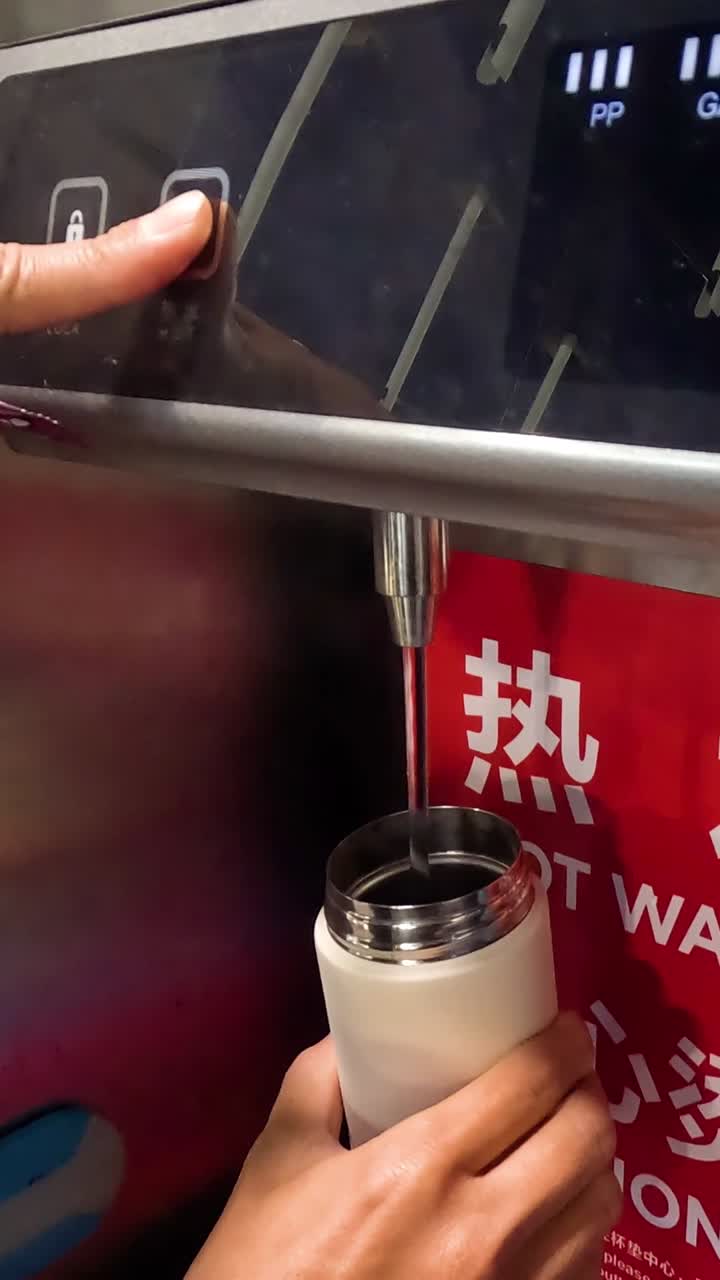Uma mão segura uma garrafa branca enquanto pressiona um botão digital em um dispensador de água