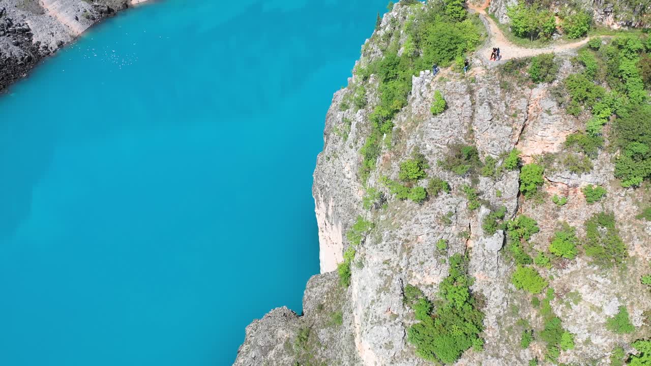 Group of people walk winding road by cliff and Blue Lake, Imotski