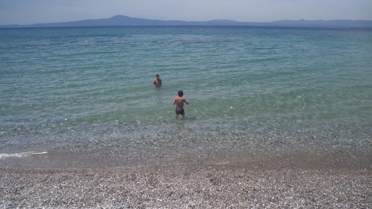 широкий вид, наклон вниз, снимок двух кавказских греческих братьев, наслаждающихся чистыми голубыми водами каламаты, пелопоннес, греция 4к