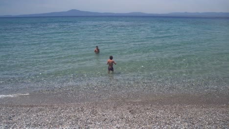 Wide-view,-tilt-down-shot-of-two-caucasian-greek-brothers-enjoying-the-clear-blue-waters-of-Kalamata,-Peloponnese,-Greece-4K