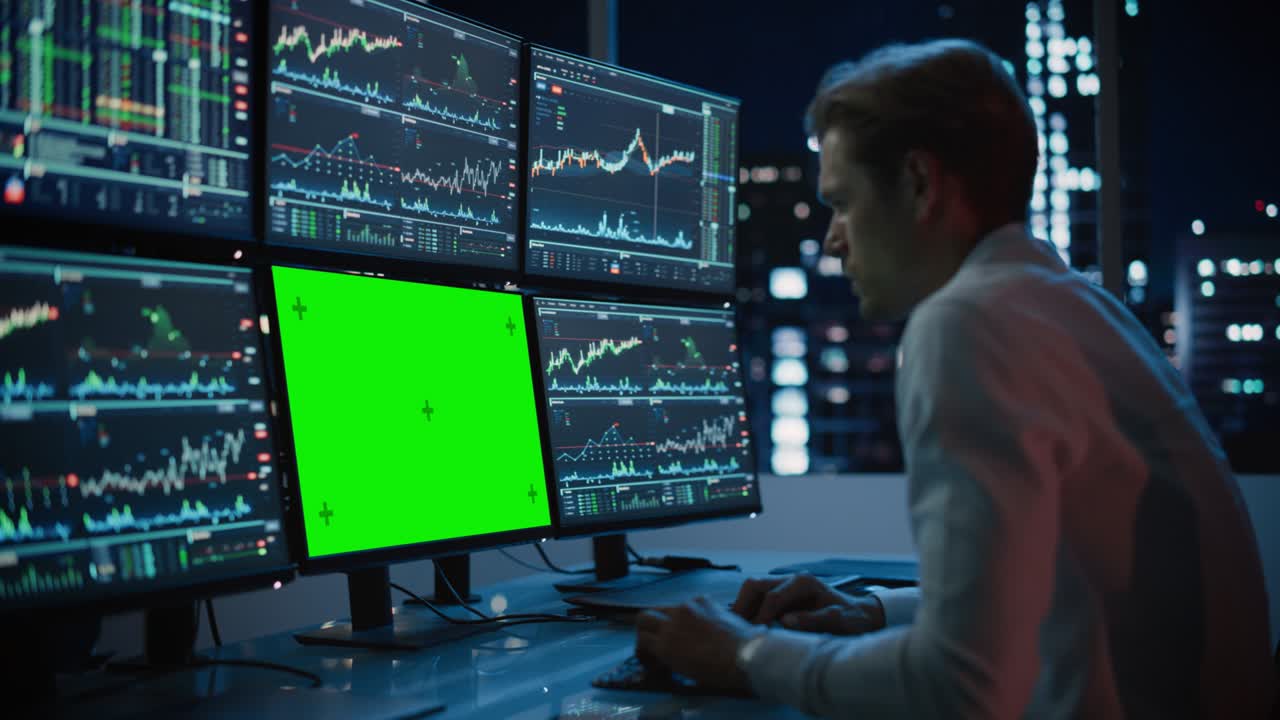 Financial Analyst Working on Computer with Multi-Monitor Workstation with Green Screen Chroma Key Mock Up Template and Real-Time Stock Charts. Businessman Works in Investment Bank in the Evening.