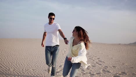 Couple-holding-hands-running-having-fun-under-sun-in-playful-and-romantic-relationship-under-sun-and-blue-sky-in-desert.-Two-young-lovers-cheerful-together-on-romance-in-summer.-Wearing-casual-clothes