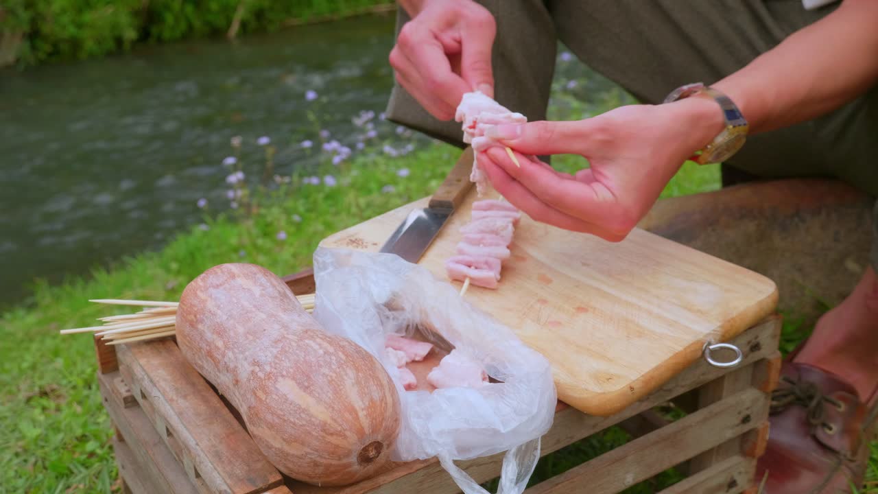 강가에서 바비큐 피크닉을 위해 고기 꼬치를 조립하는 사람의 클로즈업