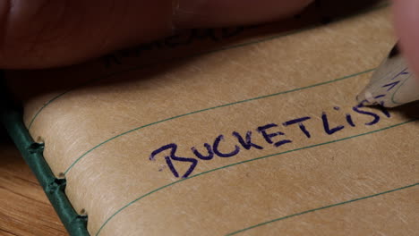 person hand writing bucket list on notebook page, close up view