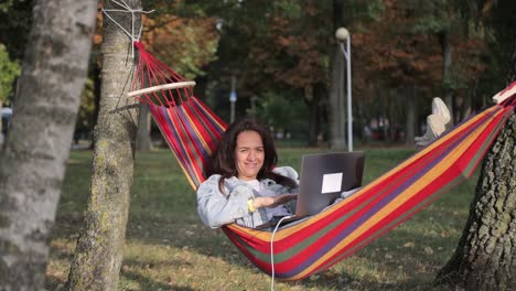 woman working on a laptop in a hammock in a park