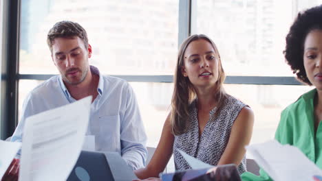 Multi-Cultural-Business-Team-Meeting-Around-Office-Boardroom-Table-With-Laptops-Discussing-Documents