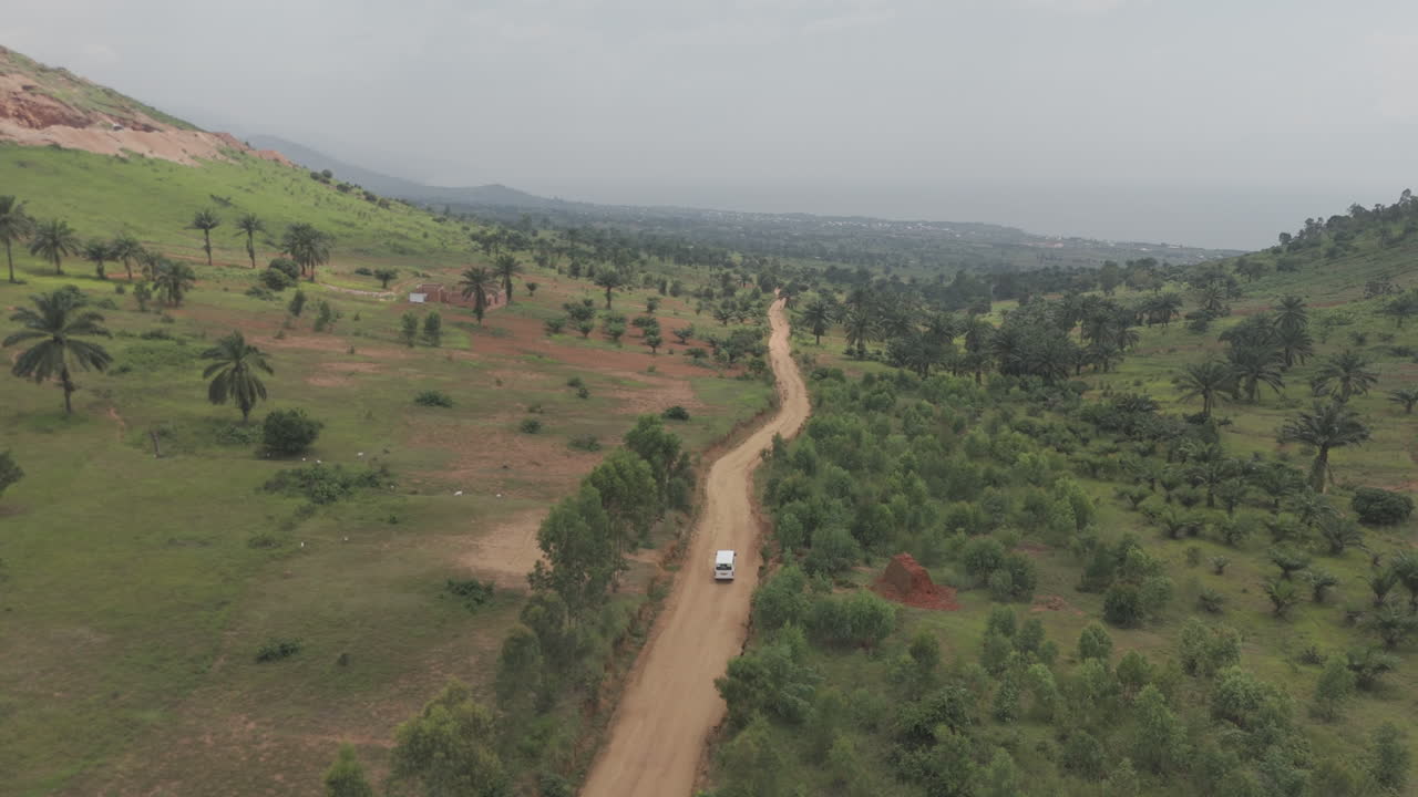 Following drone shot of a white bus or van driving on a rocky road near the town of Kimina Bujumbura Burundi Africa on a warm day with the landscape in the back LOG
