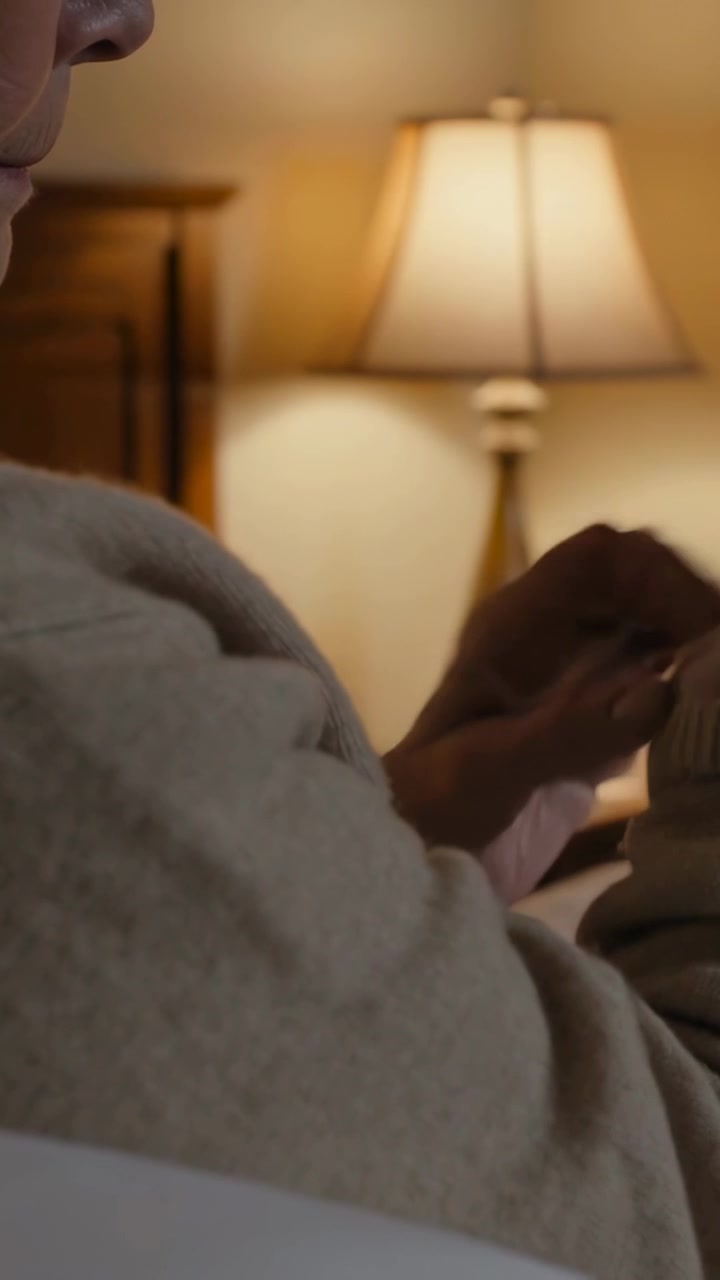 Vertical video: Offering arm as senior in knit sweater helping fix clasp at bed by lamp, copy space