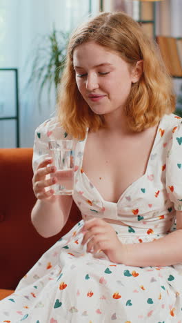 thirsty young woman sitting at home holding glass of natural aqua make sips drinking still water