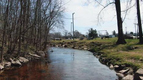 toma de reenvío sobre un canal de agua en un campo rural con bosque seco en un lado y un parque infantil en el otro lado en la ciudad de mishicot, condado de manitowoc, centro este de wisconsin, estados unidos
