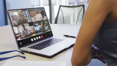 African-american-woman-using-laptop-for-video-call,-with-diverse-business-colleagues-on-screen