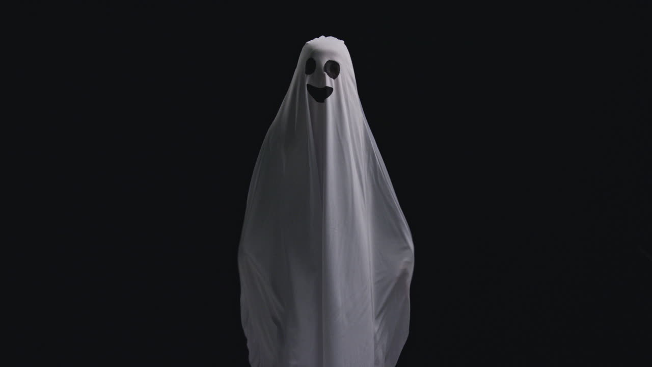 Child Dressed Up In Ghost Costume Trick Or Treating At Halloween Scaring People Against Black Background