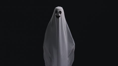 Child-Dressed-Up-In-Ghost-Costume-Trick-Or-Treating-At-Halloween-Scaring-People-Against-Black-Background