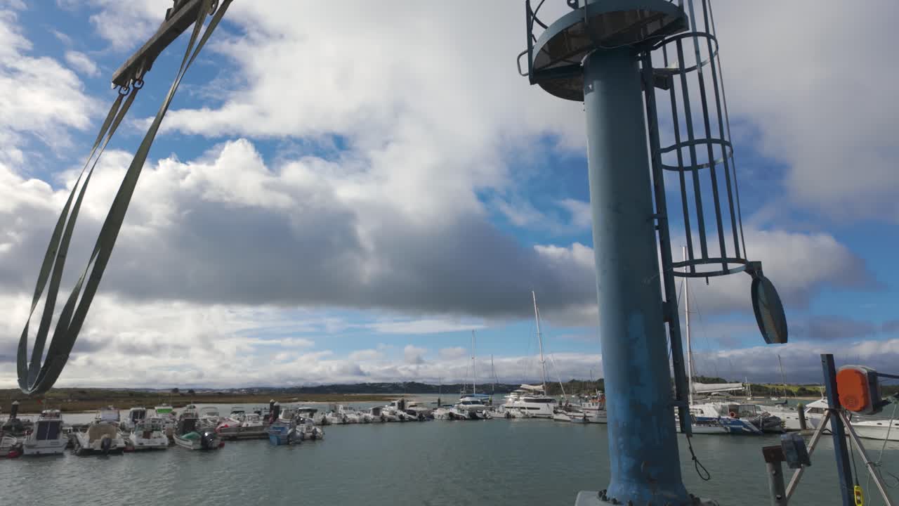 Blue boat lifting crane at the fishing harbour in Alvor, Algarve, Portugal, with moored boats
