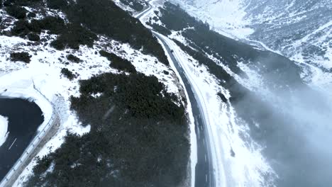 aerial view of a small car driving on a snow covered mountain road during a cloudy winter day with snowfall in switzerland