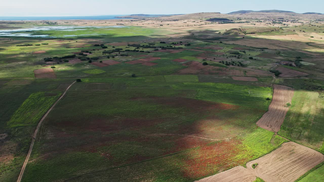 Large clouds cast huge dark shadow above speckled green orange red grassland farm plots in countryside