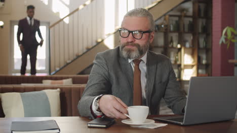 Senior-Businessman-Drinking-Coffee-and-Working-on-Laptop-in-Restaurant