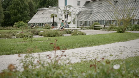 Young-man-sitting-on-a-bench-in-a-small-par-near-a-house-in-cloudy-summer-day