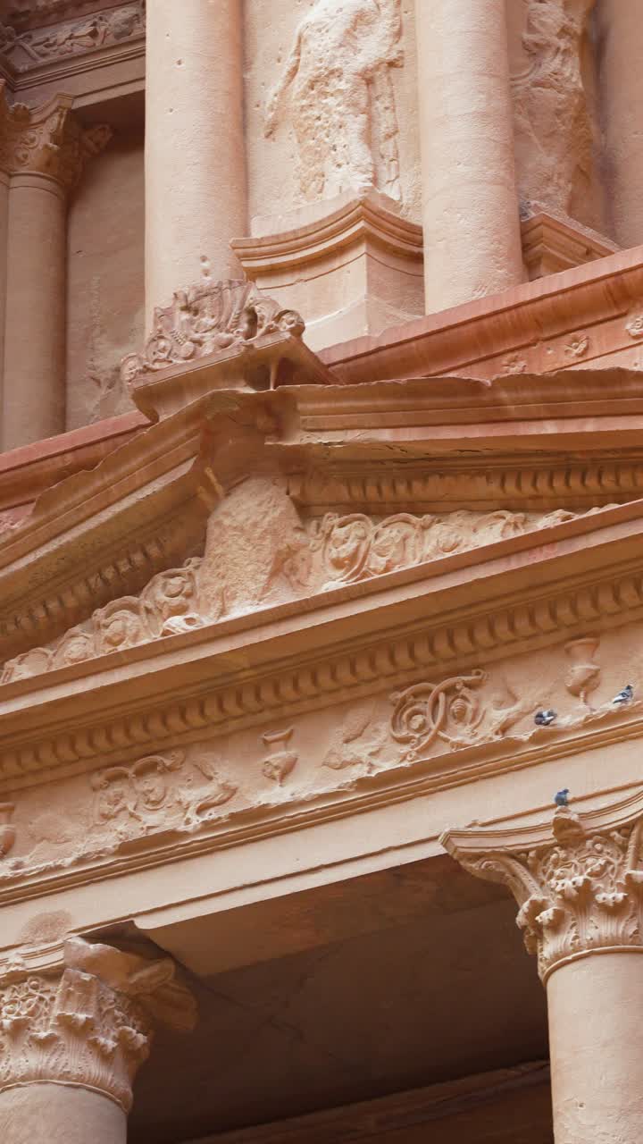 Panoramica verticale cinematografica attraverso la facciata scolpita di Al Khazneh a Petra, Giordania, che rivela colonne in arenaria, dettagli ornamentali e antica maestria architettonica.