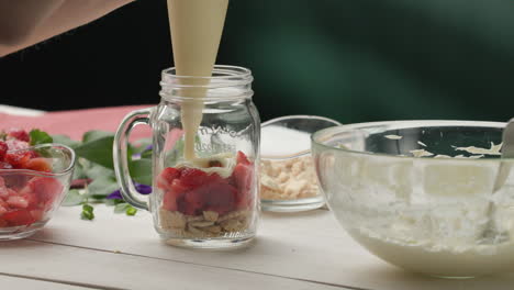 assembling dessert - using pastry bag to apply layer of whipped cream onto macerated strawberries and gentle shaking to spread evenly