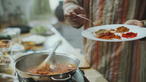 chef sprinkling aromatic spices into simmering tomato sauce in pan