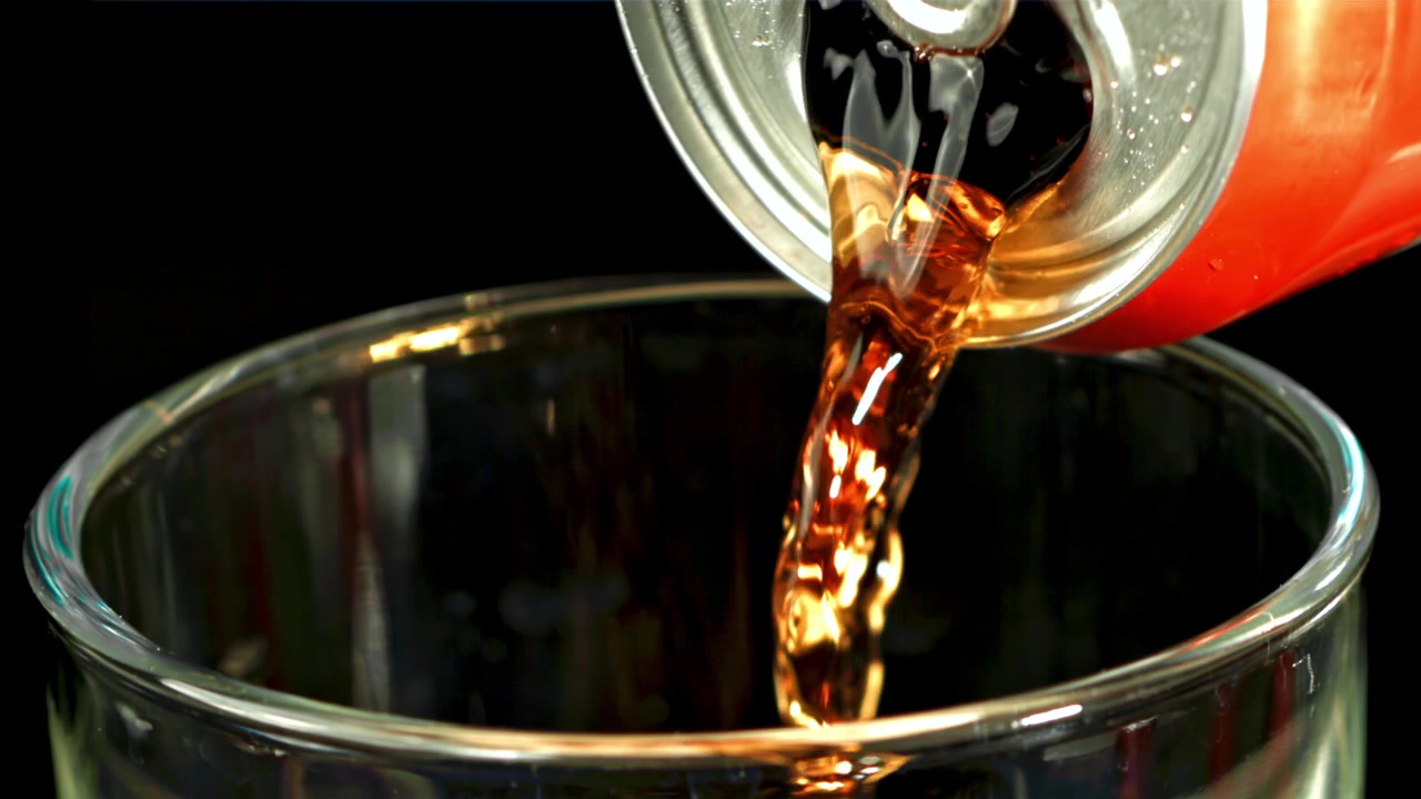 Versamento al rallentatore di cola da una lattina rossa in un bicchiere