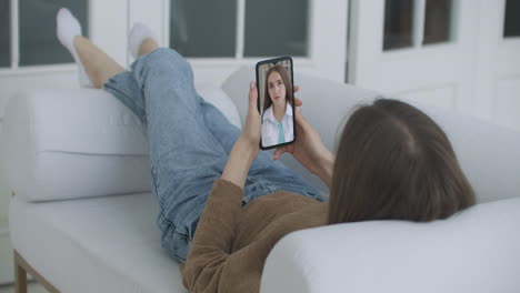 Mujer-Joven-Enferma-En-Casa-Usando-Un-Teléfono-Inteligente-Para-Hablar-Con-Su-Médico-A-Través-De-Una-Aplicación-Médica-De-Videoconferencia.-La-Mujer-Tiene-Una-Conversación-Con-Un-Médico-Profesional-Utilizando-Una-Aplicación-De-Video-Chat-En-Línea.