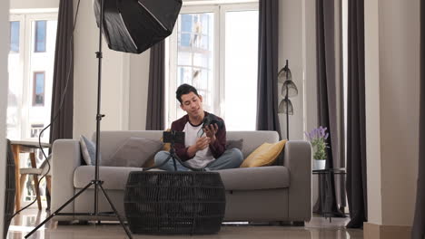 Young latin man talking on mobile camera, explaining a photo camera. Content creator concept