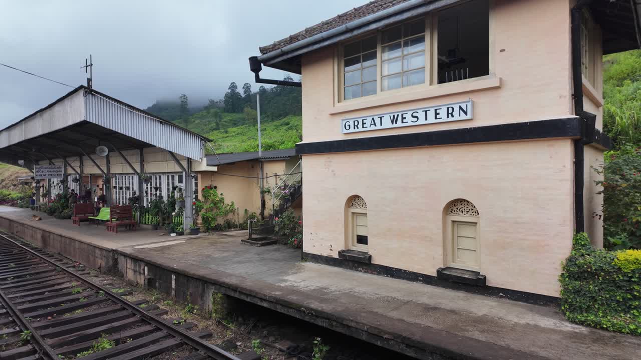 The Great Western station in Talawakelle, Sri Lanka, showcases a charming blend of rustic architecture and natural beauty, with misty hills and an overcast sky creating a tranquil atmosphere.
