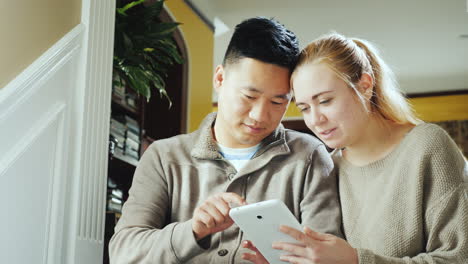 Young-Couple-Enjoys-Tablet-In-House-Sitting-On-Stairs