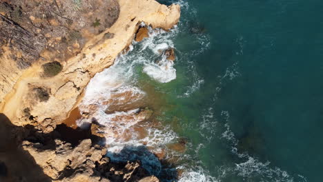 raveling aerial of the rugged coastline of portugal unfolds, as the gentle sea waves delicately embrace the rocky formations under the radiant sunshine of a delightful day